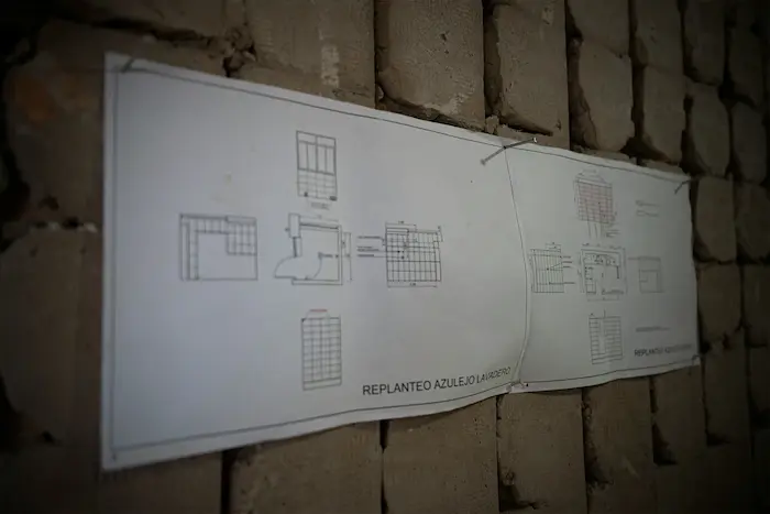 Un plan architectural affiché sur un mur en briques apparentes, montrant des schémas de disposition de pièces et des dimensions.