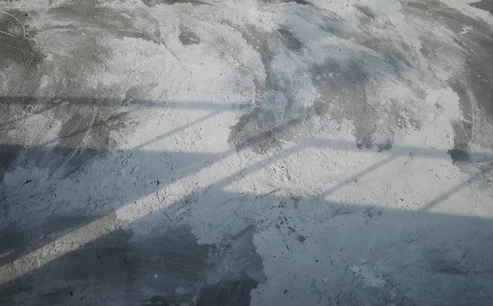 Un sol en béton brut avec des traces de peinture blanche et des ombres projetées par des objets ou des structures situées hors champ.