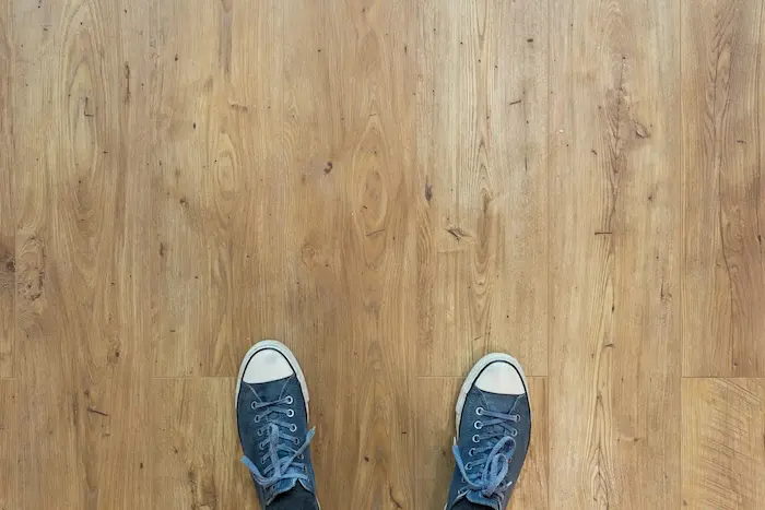 Vue de dessus de deux pieds chaussés de baskets bleues sur un sol en bois clair avec des nœuds visibles.